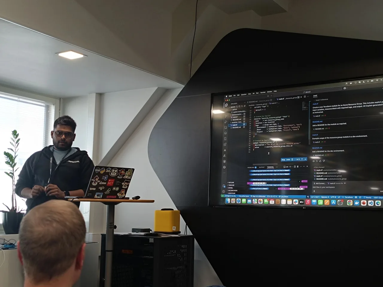 Sanket presenting at Microsoft DevXperience, with GitHub Copilot writing a Terraform module on the screen behind him